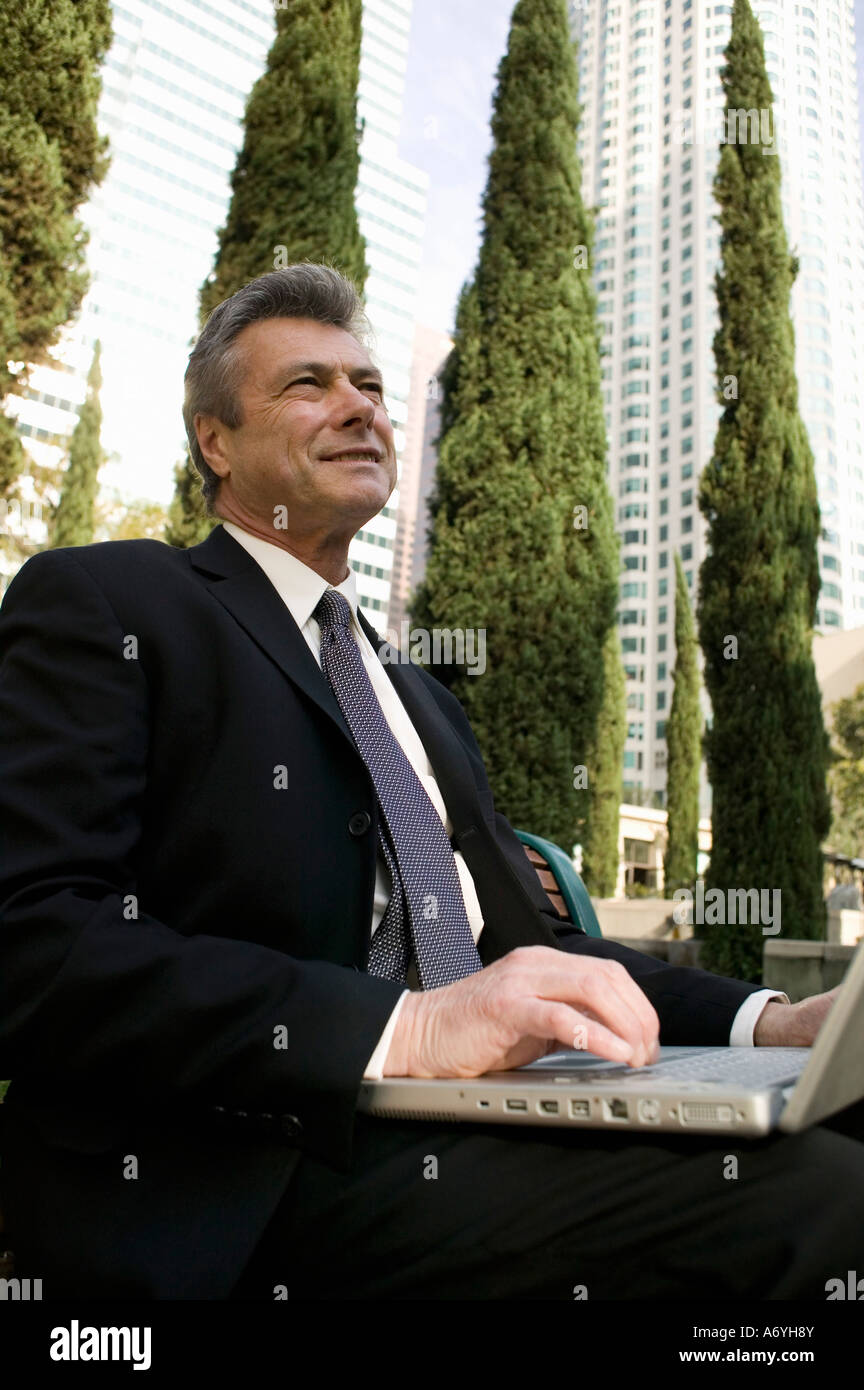 Businessman sitting on a park bench and using a laptop Stock Photo - Alamy