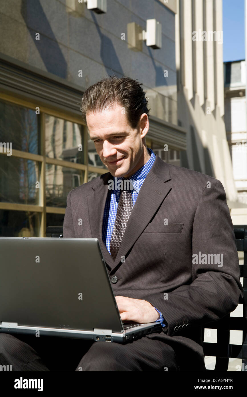 Businessman sitting on an outside bench using a laptop Stock Photo - Alamy