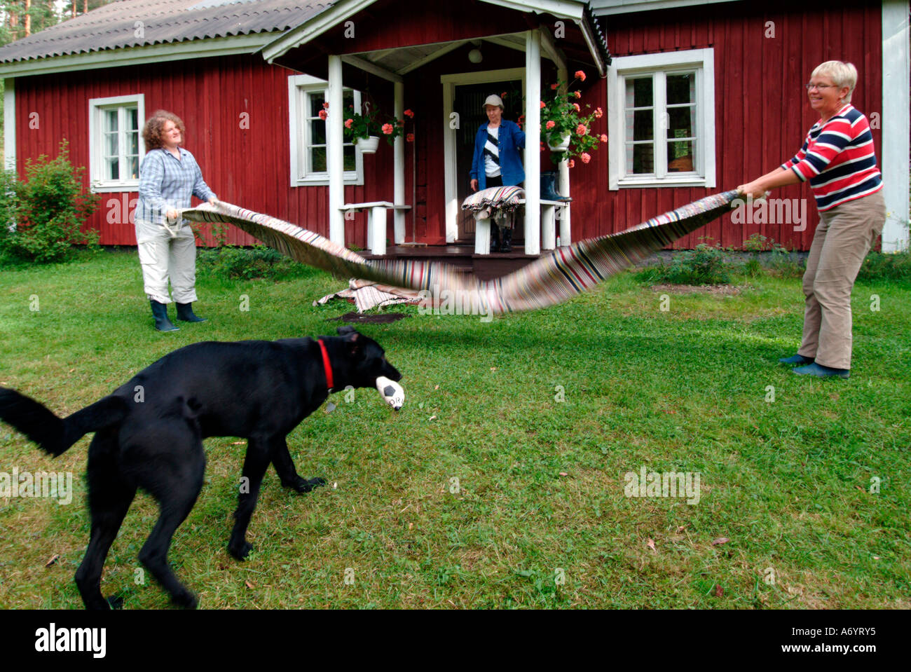 a dog in front of two women dedusting rag rugs in front of a red wooden ...