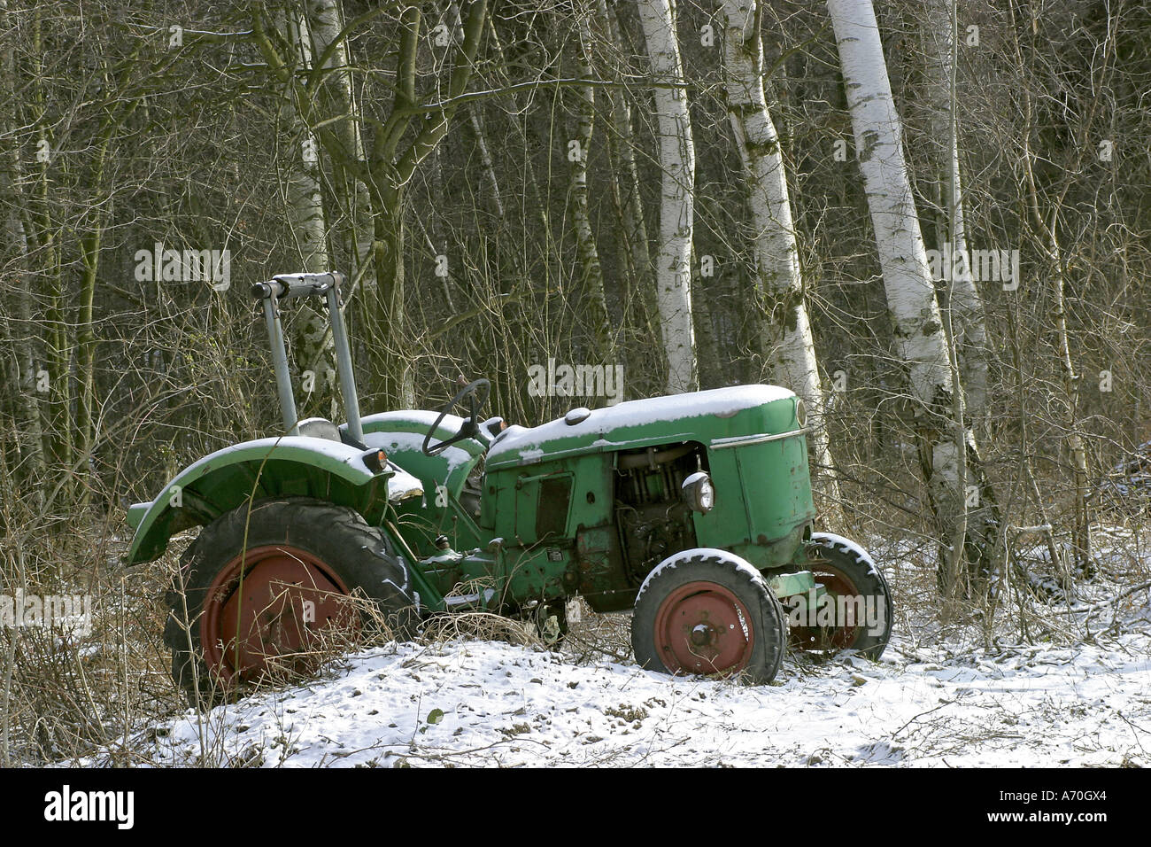 Old green Deutz vintage tractor standing forgotten in snow at the edge of a forest Stock Photo