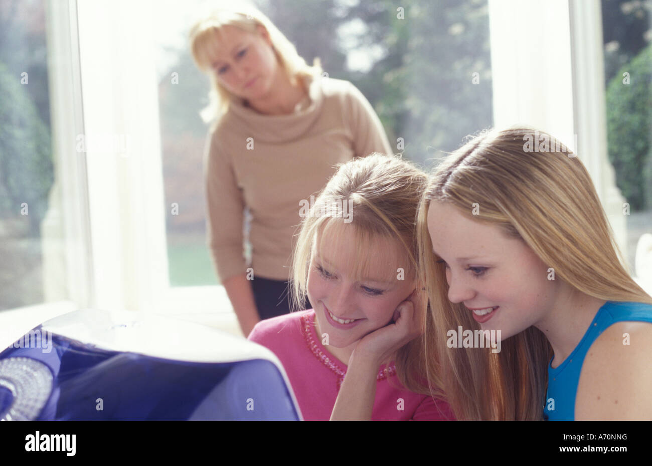 teenage girls on computer with concerned mother in the background Stock Photo