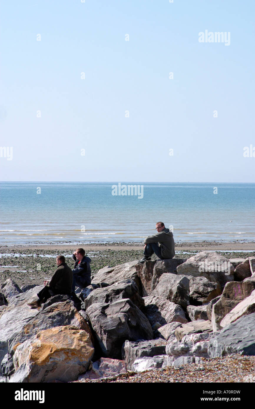 Three young men sitting on rocks on beach at GoringbySea, West Sussex