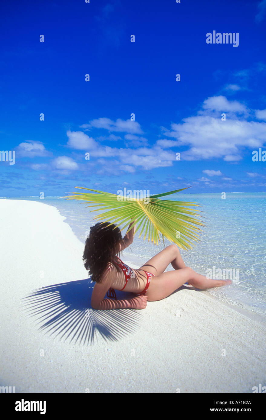 Woman in bikini sitting on beach under palm frond in Aitutaki Lagoon Cook Islands South Pacific Ocean model released image Stock Photo