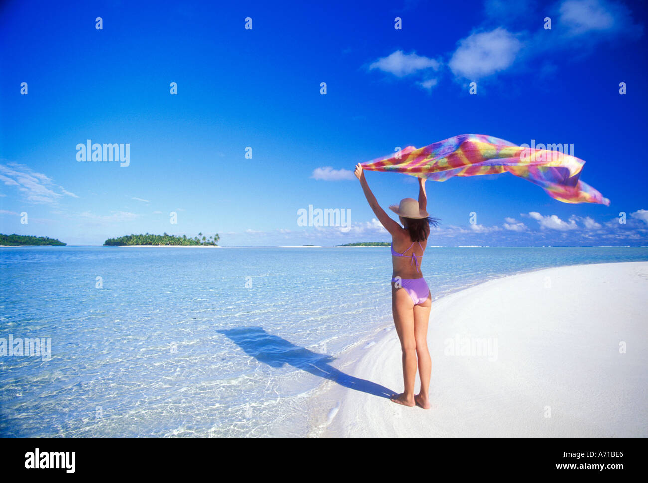 Woman in swimsuit holding Polynesian pareau overhead for shade in Aitutaki Lagoon in the Cook Islands South Pacific Ocean Stock Photo