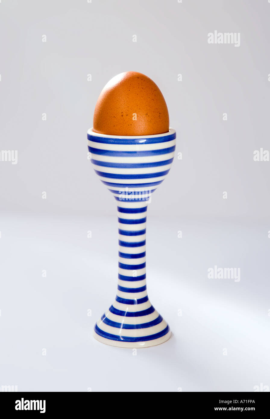 A boiled egg in a blue and white stripey egg cup on white background. Stock Photo