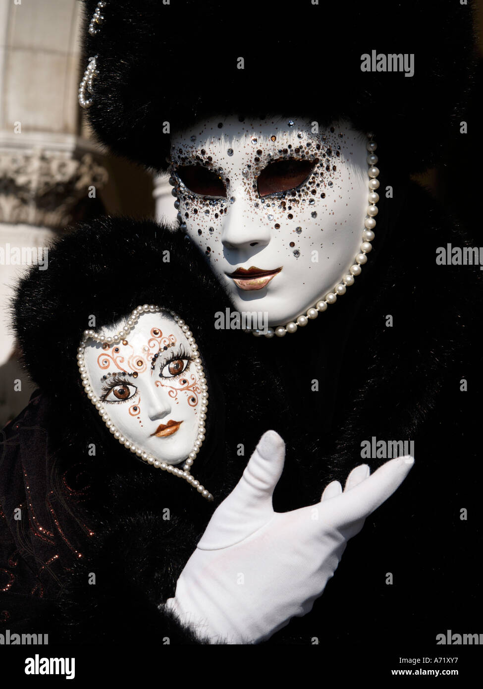 character in white mask holding small mask at Venice carnival Stock
