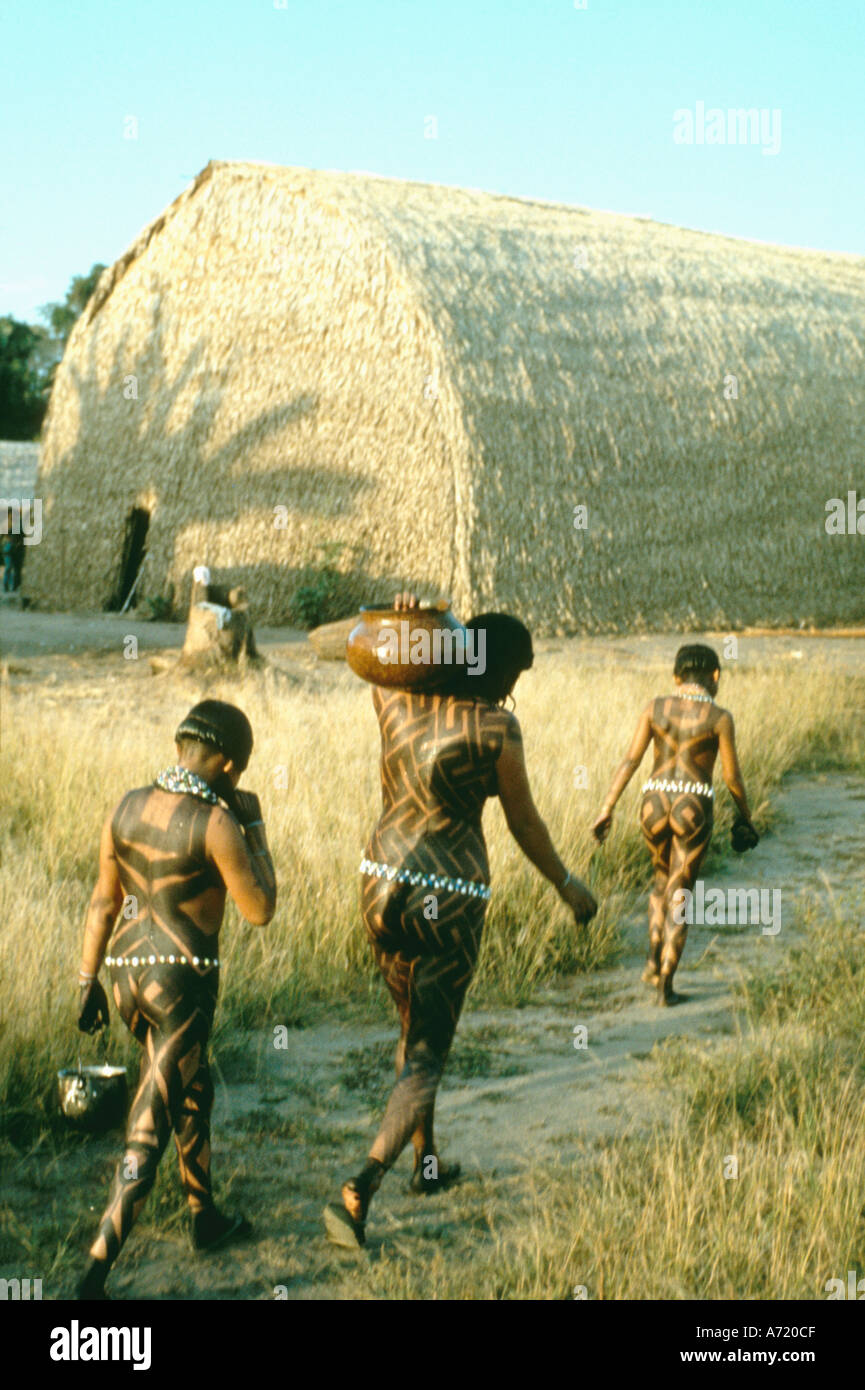 Three female Asurinin Indians bodies painted in genipa dye carrying jugs of water from the river middle Zingu region Brazil Stock Photo