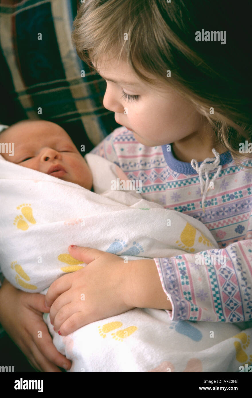 Young girl holding her new born baby brother who is swaddled in a