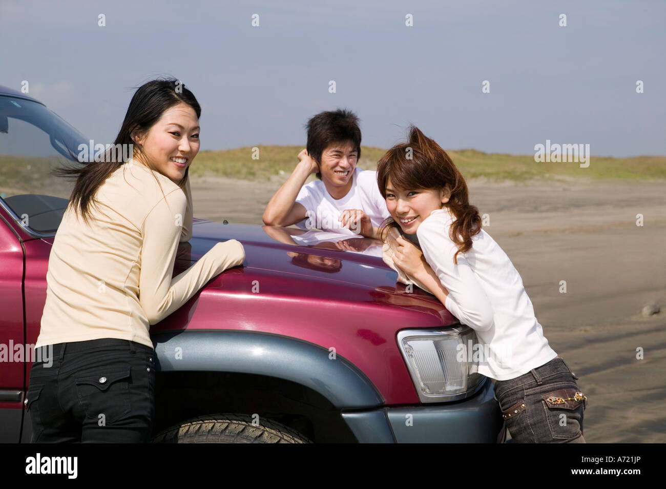 Young people leaning against car on beach Stock Photo - Alamy