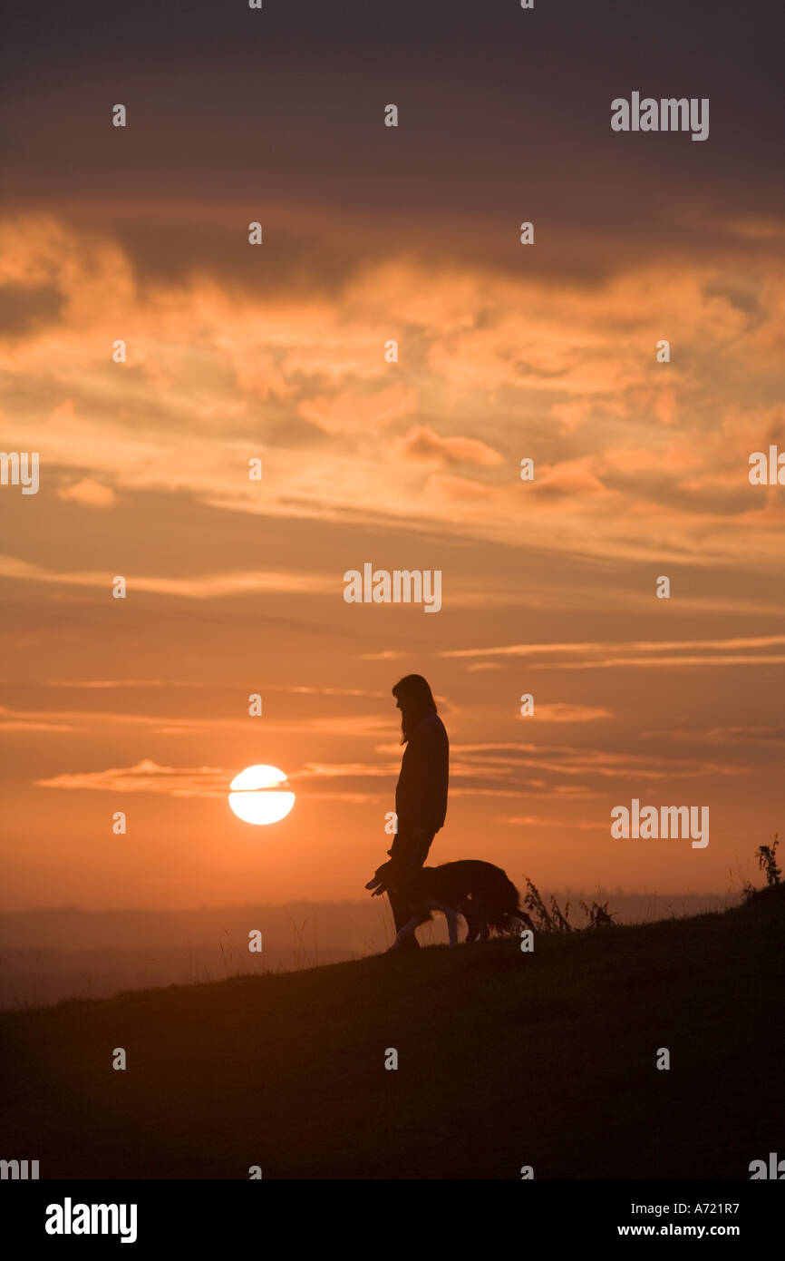 Lone woman walking a Border Collie on a hillside with the sun setting