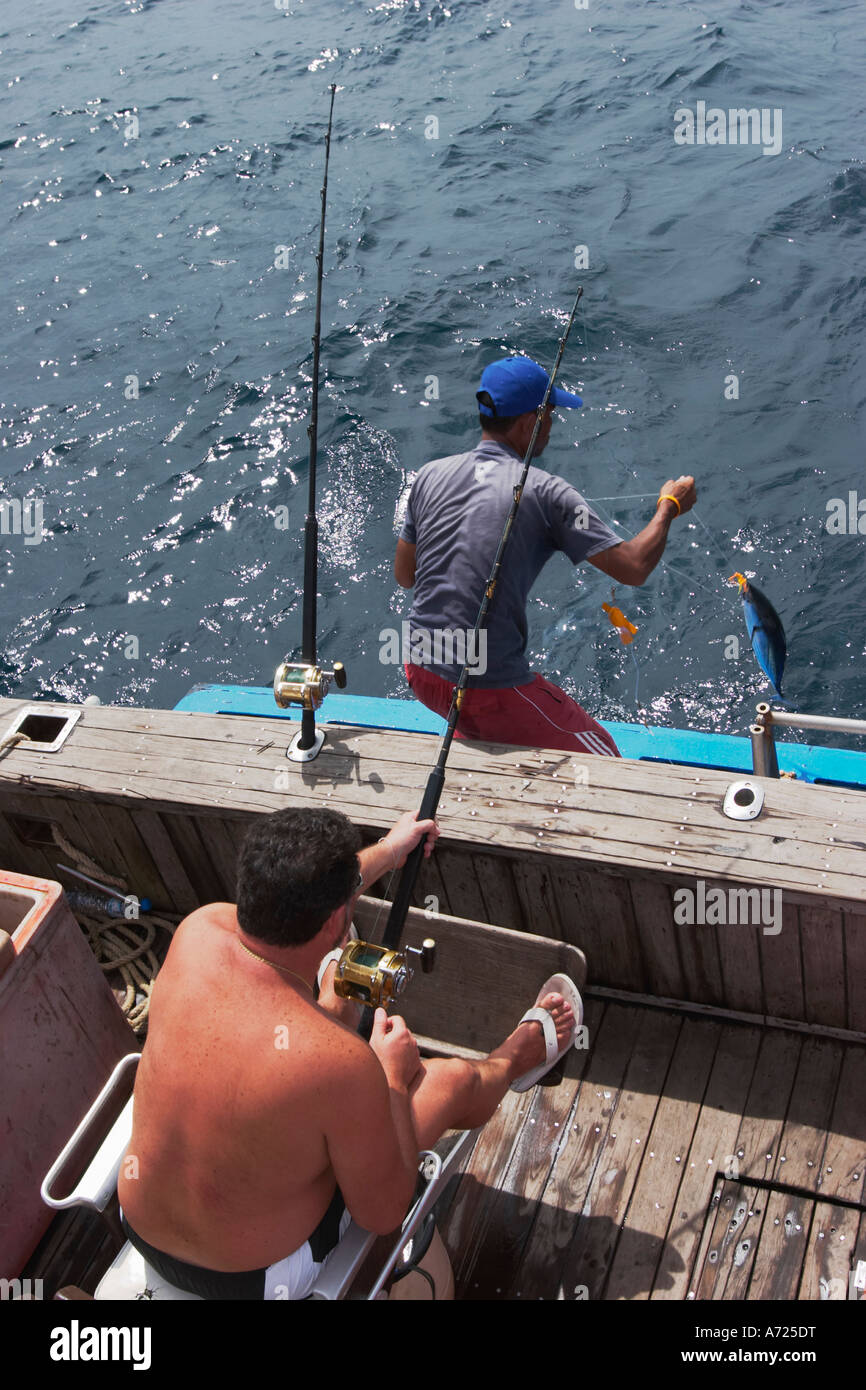 Thai fishing guide helping tourist fisherman to raise hooked tuna on board. Phuket island, Thailand. Stock Photo