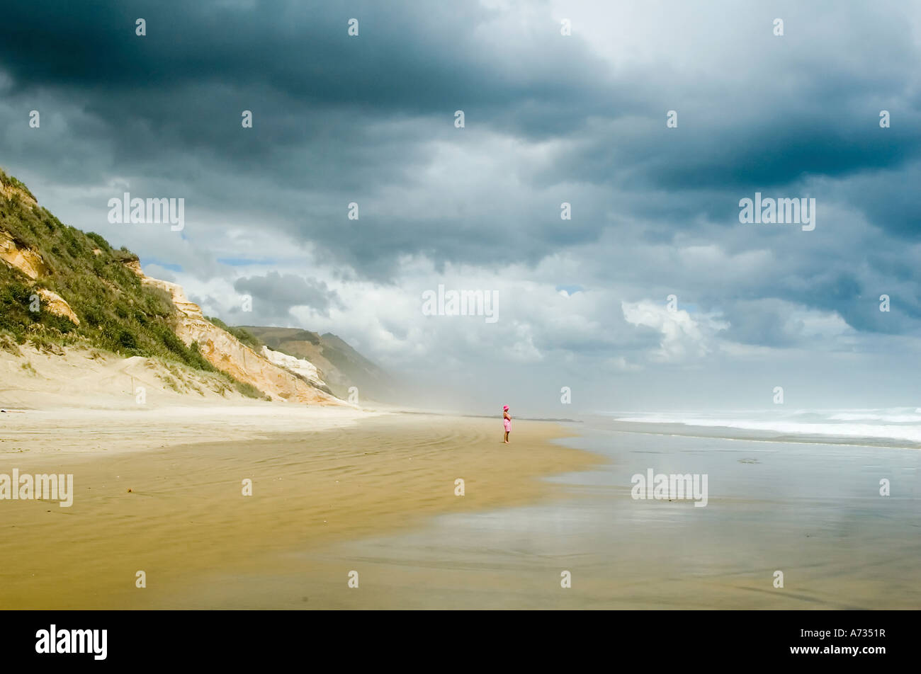 A woman in a pink bathing suit stands alone on ninety mile beach.  New Zealand. Stock Photo