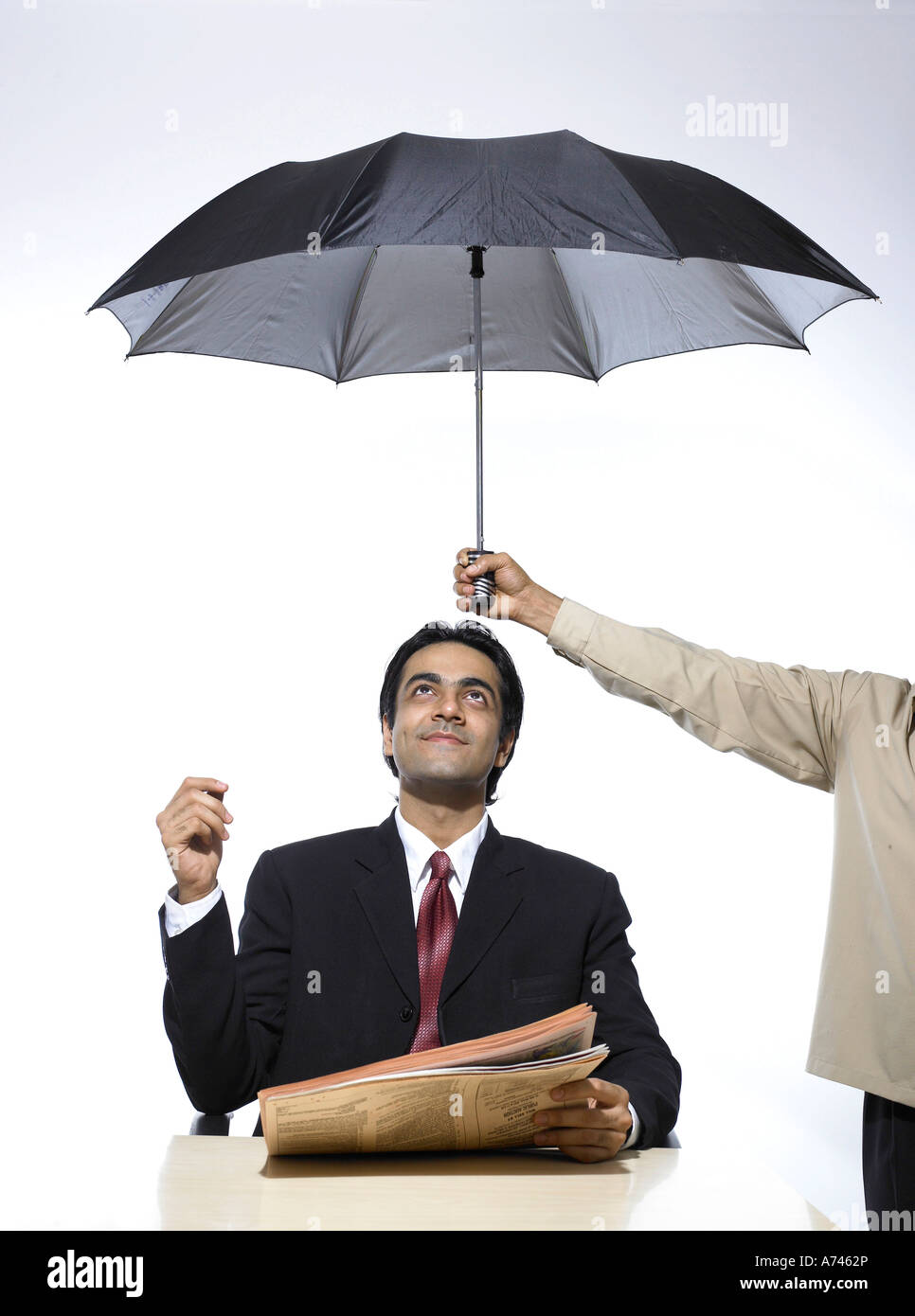 VDA 201900 South Asian Indian executive holding newspaper sitting under umbrella looking above MR 702A Stock Photo