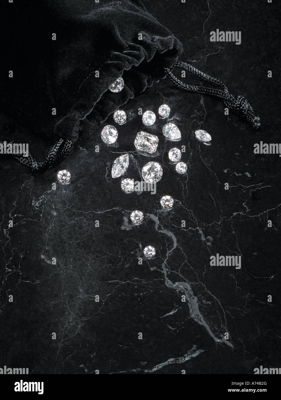 Diamonds of various shapes and sizes slip from their black velvet bag onto a marble surface Stock Photo