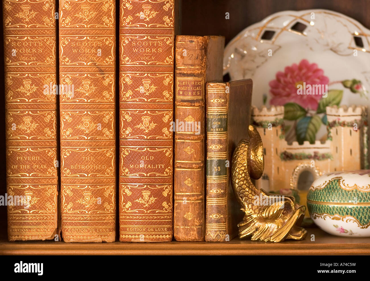 Collection of antique books on a shelf with china and brass knick