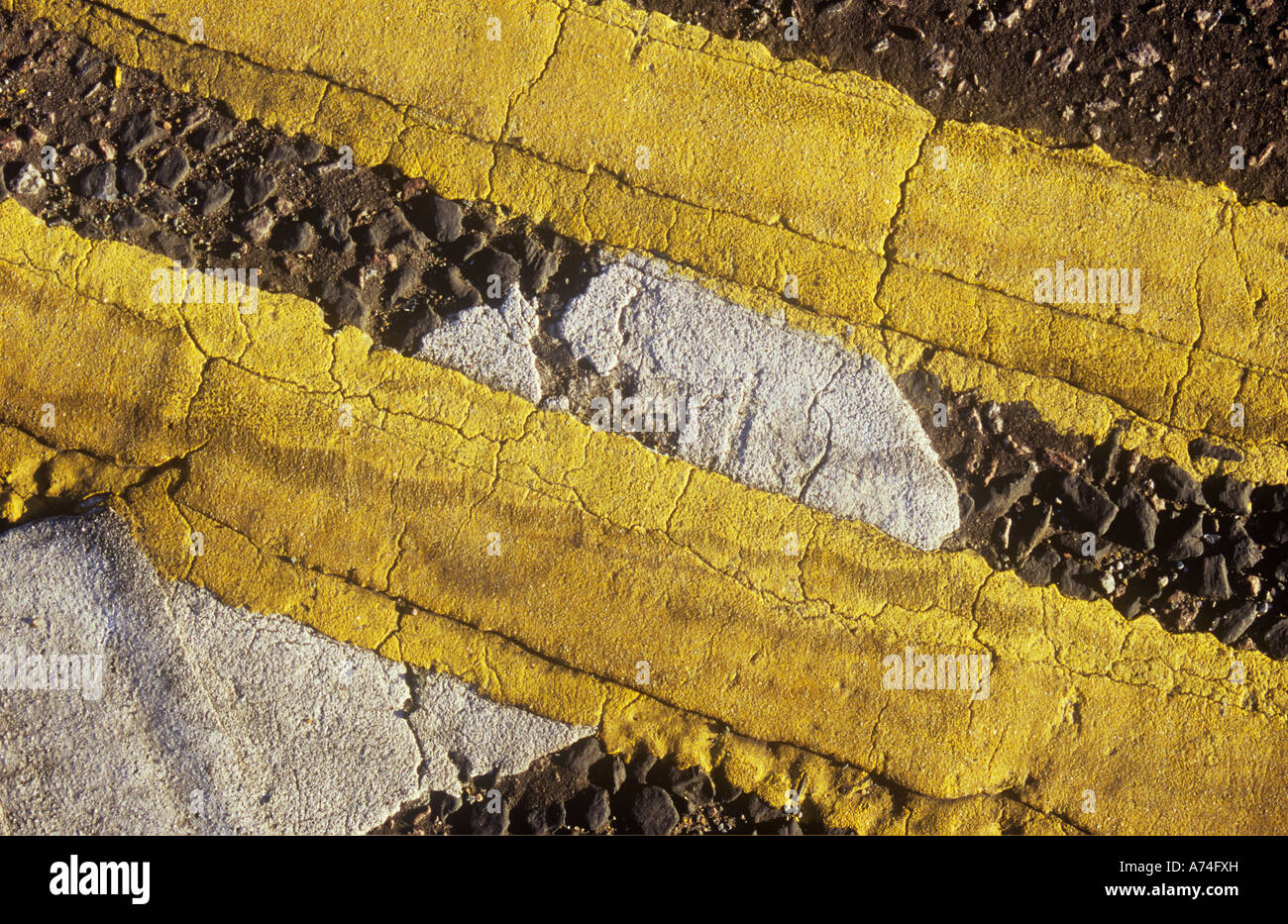 Detail of ragged-edged and cracked double yellow lines on slight curve and traversing white Give Way line Stock Photo