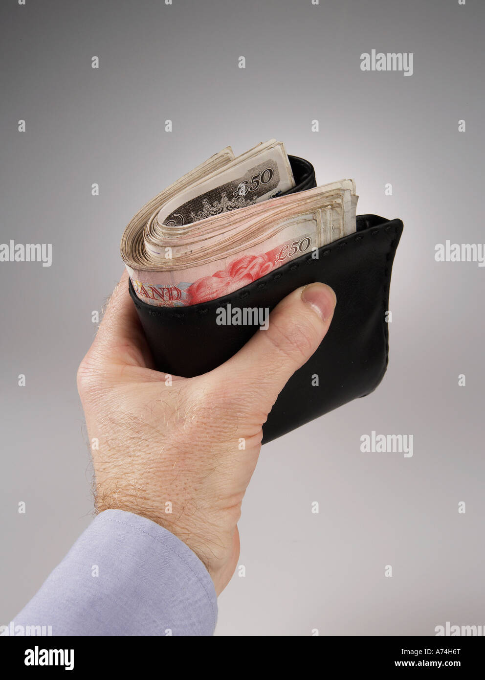 mans hand holding wallet stuffed with five thousand british pounds, in