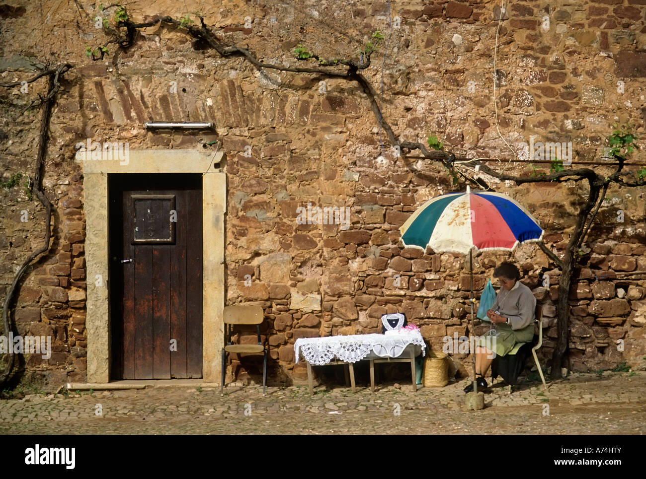 Woman knitting and selling lace in street sitting in shade under umbrella Silves Algarve Portugal Stock Photo