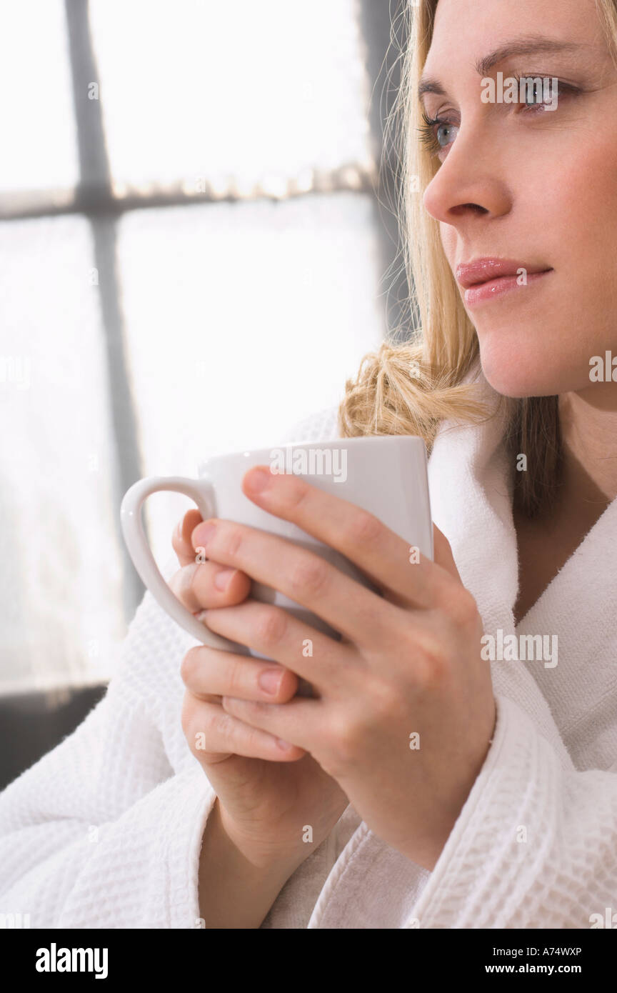 portrait of thoughtful young woman in bathrobe holding mug Stock Photo