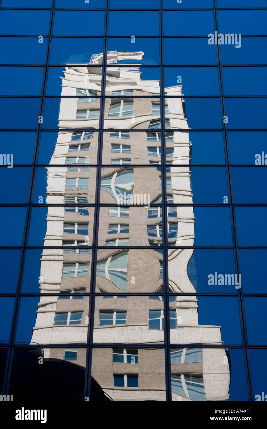 tall building reflected in anothers panes of glass on bright sunny day with blue sky Stock Photo