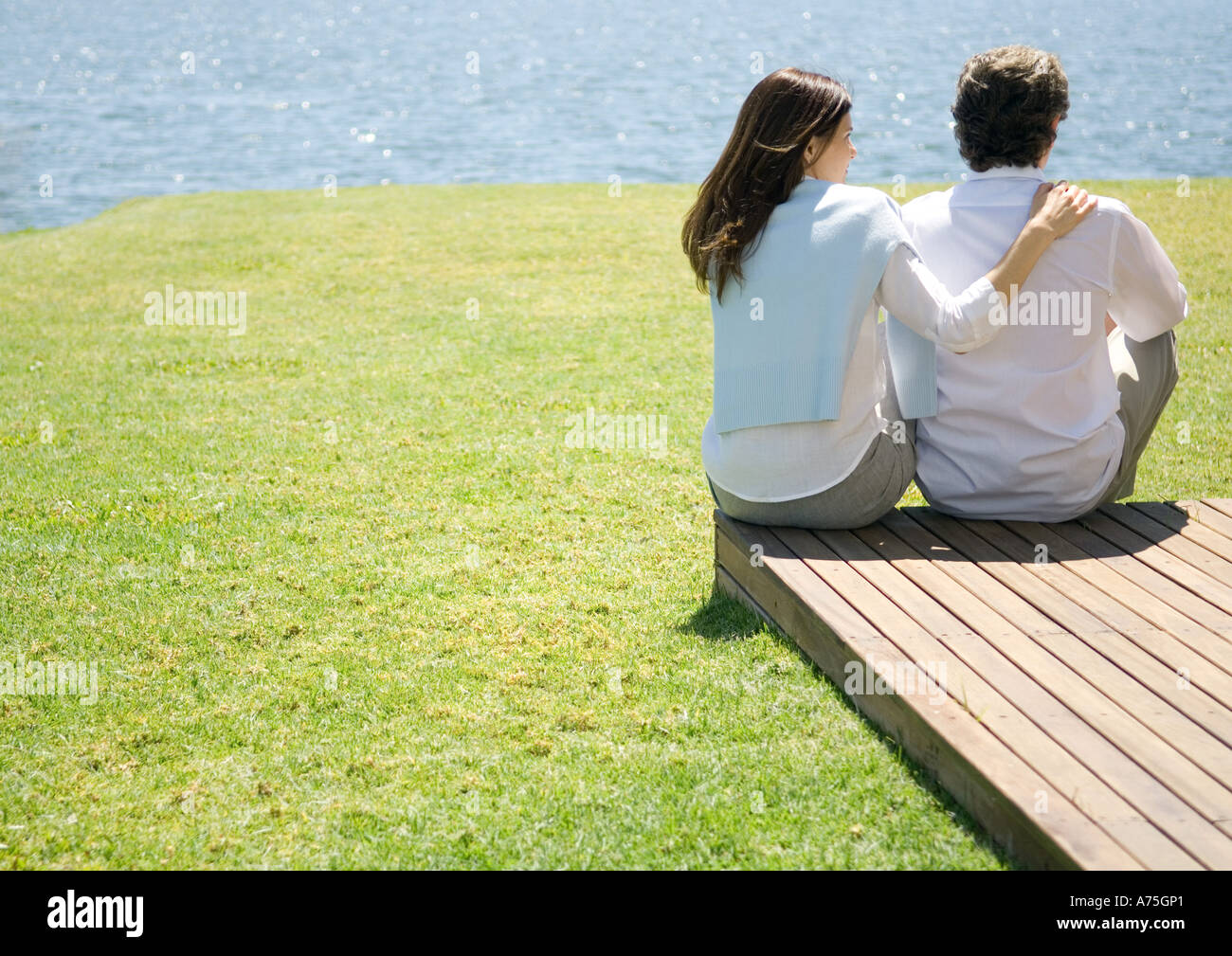 Mature couple sitting at end of wooden walkway, near water Stock Photo