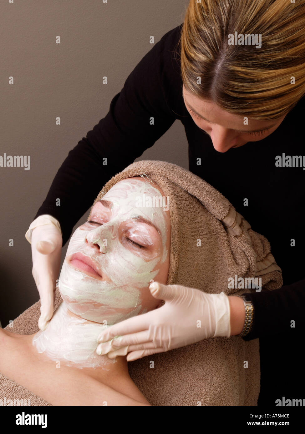 Female beautician applying skincare light green beauty mask to woman using surgical gloves Stock Photo
