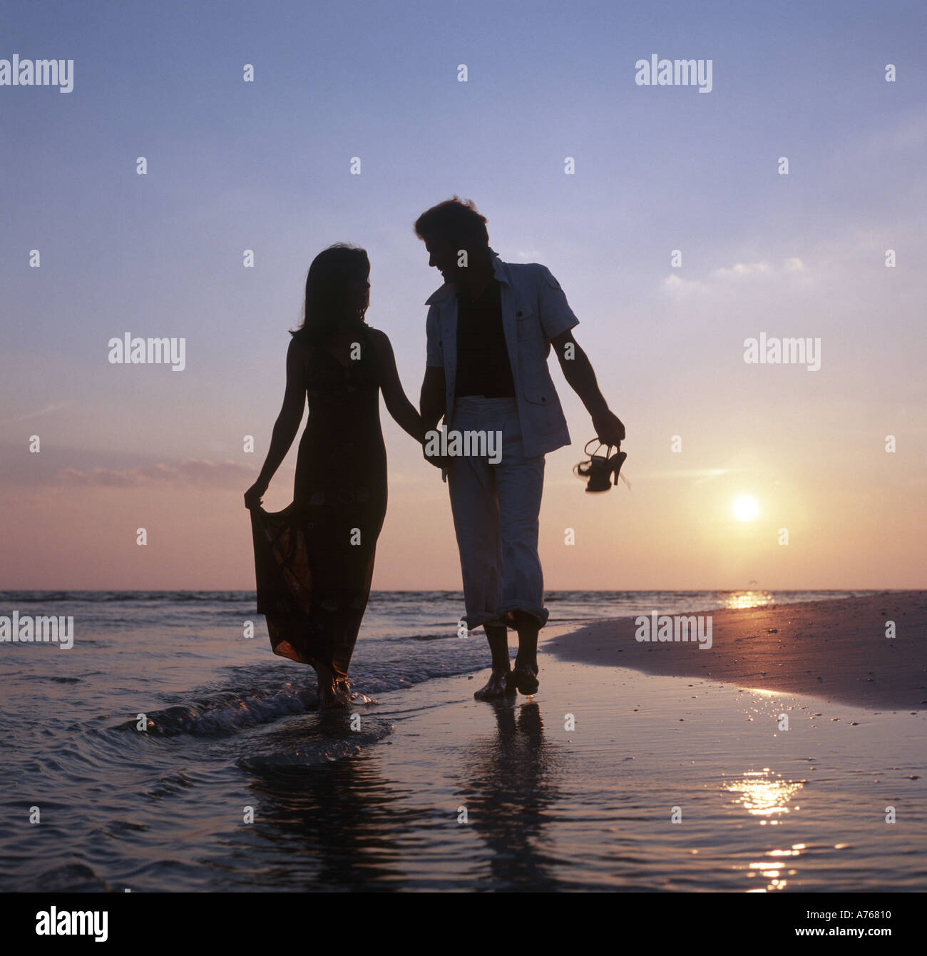 couple in evening clothes strolling on beach at sunset Stock Photo