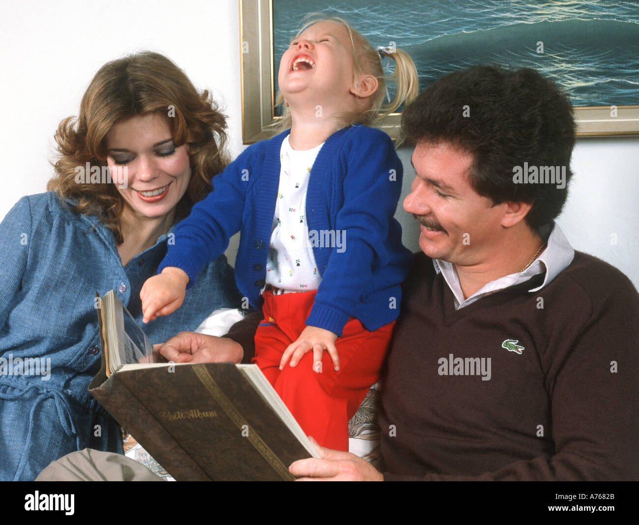 family of three looking at family album in home Stock Photo