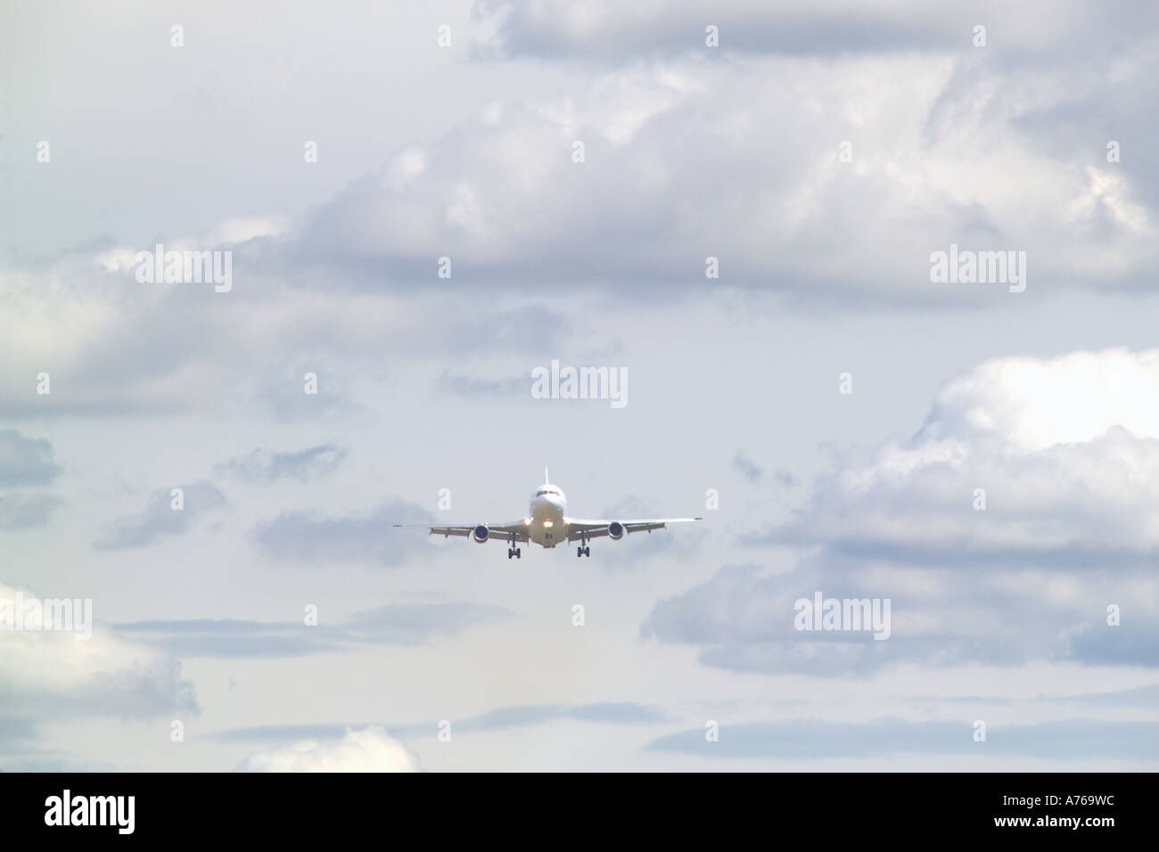 A passenger jet aircraft coming in to land viewed from the front with a cloudy sky. Stock Photo