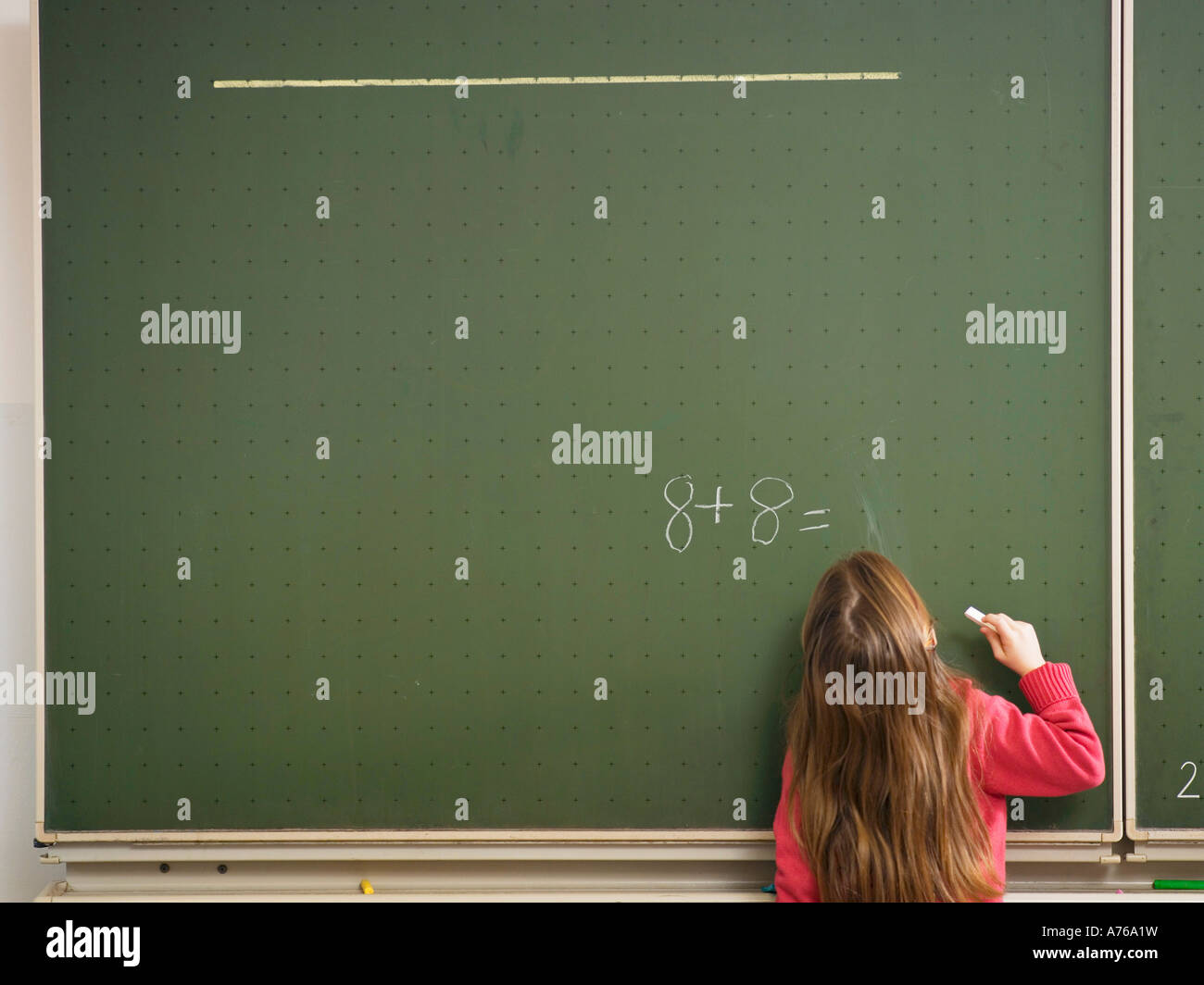 Girl standing in front of blackboard, solving arithmetic problem, rear ...