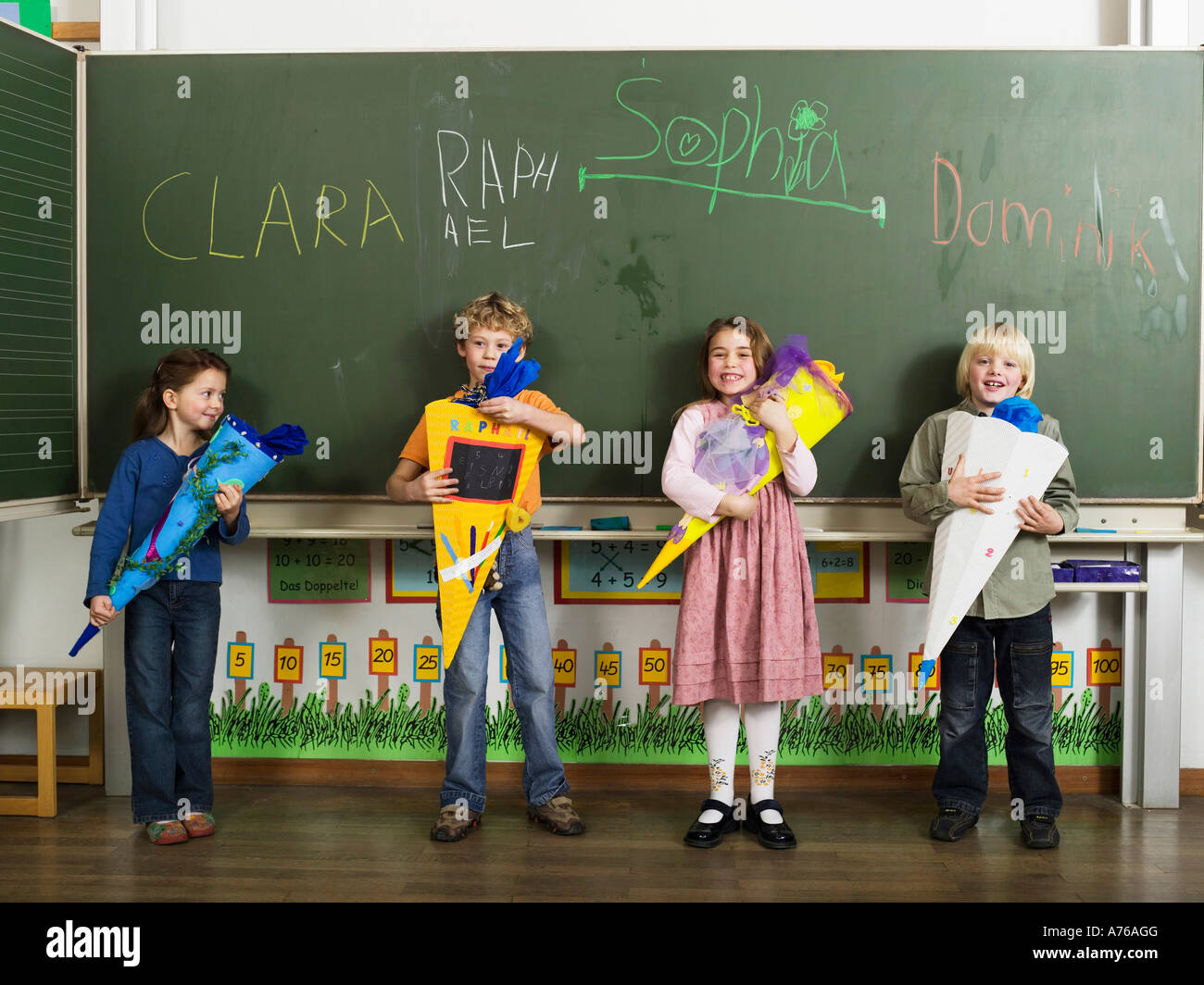 Children (4-7) standing in front of blackboard holding school cones Stock Photo