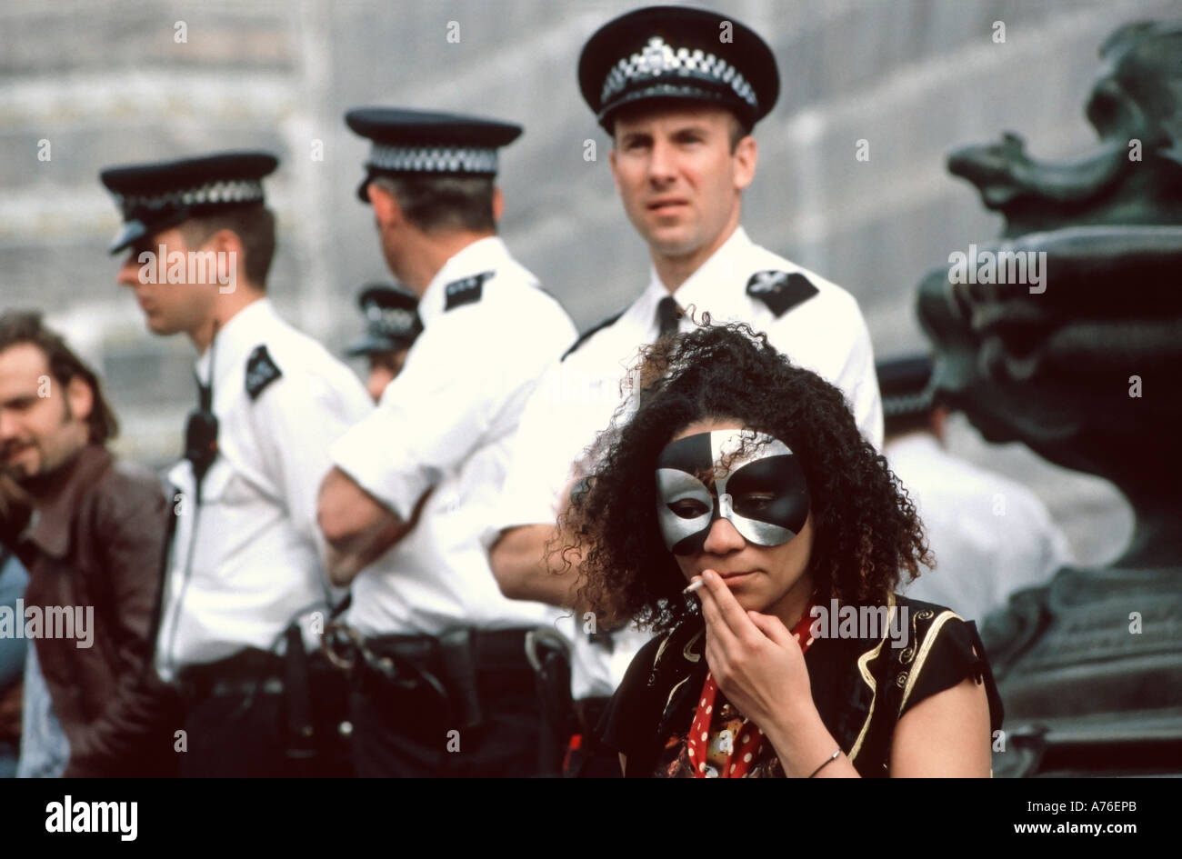 Defiant demonstrator smoking a spliff or joint with a row of police officers behind during the May Day demonstrations. Stock Photo