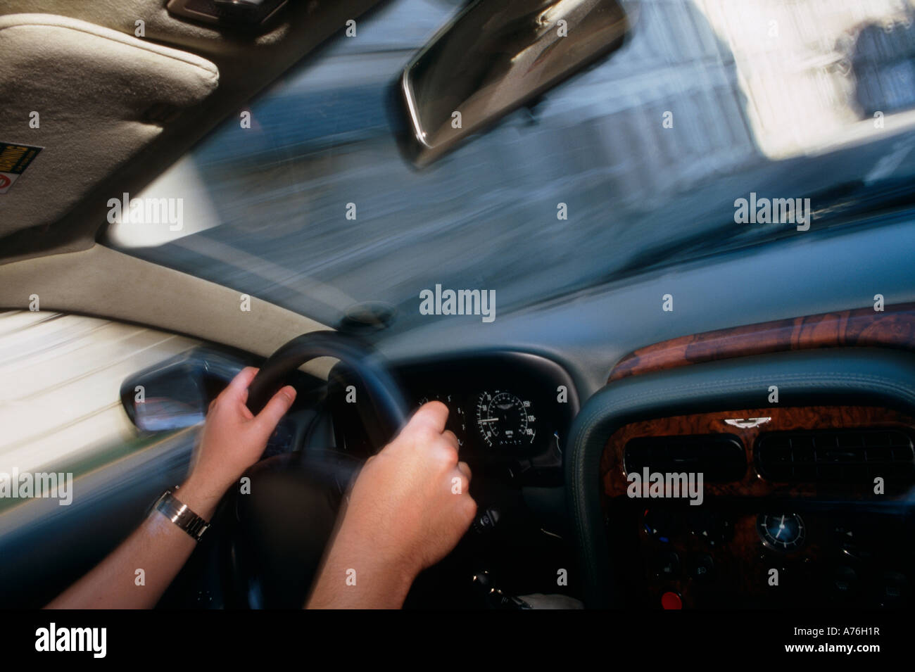 Interior of Aston Martin DB7 Vantage looking across steering wheel and drivers hands and being driven at speed Stock Photo