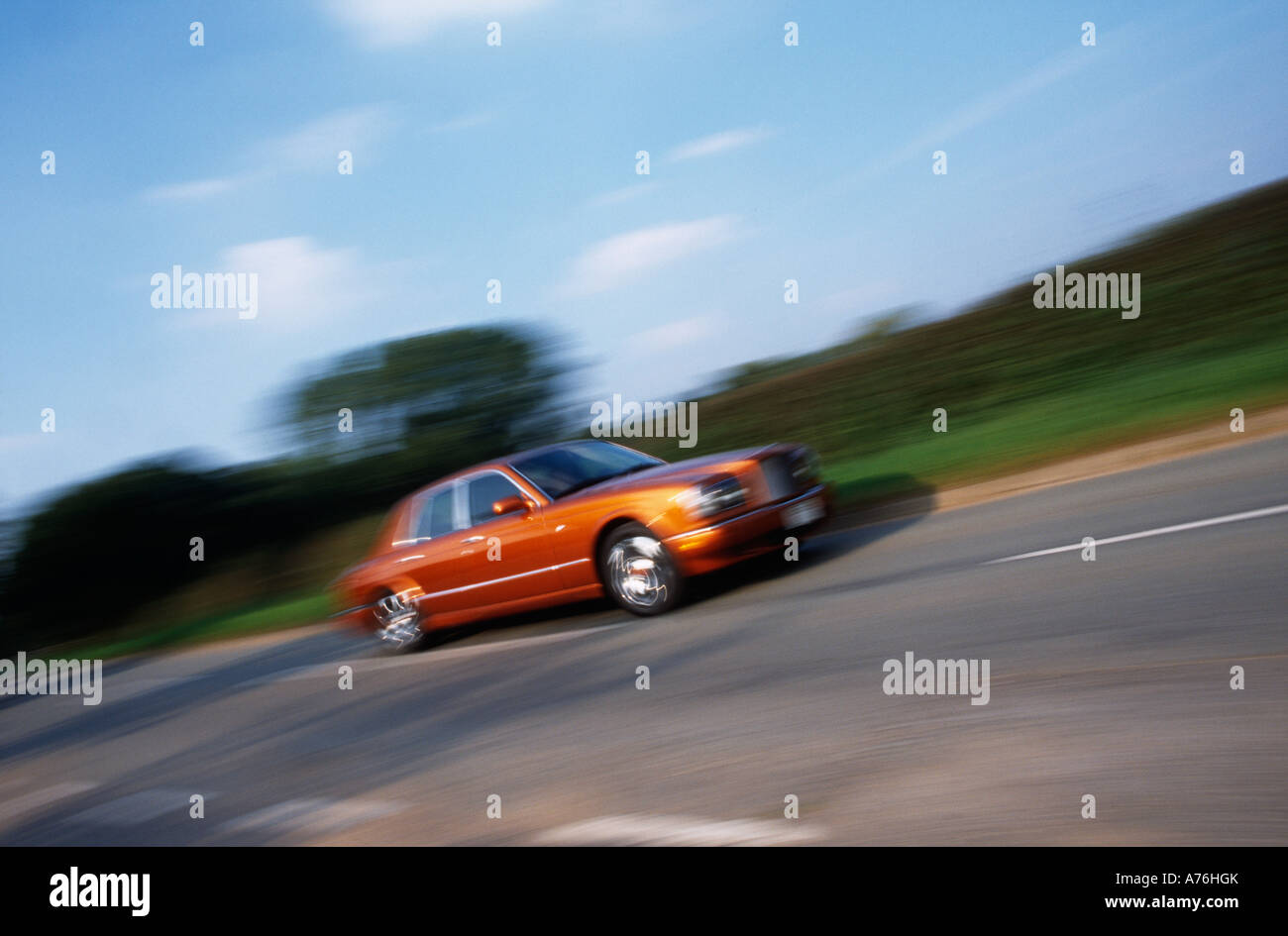 Panning shot of bronze coloured Bentley Arnage Red label driving at speed along a country road Stock Photo