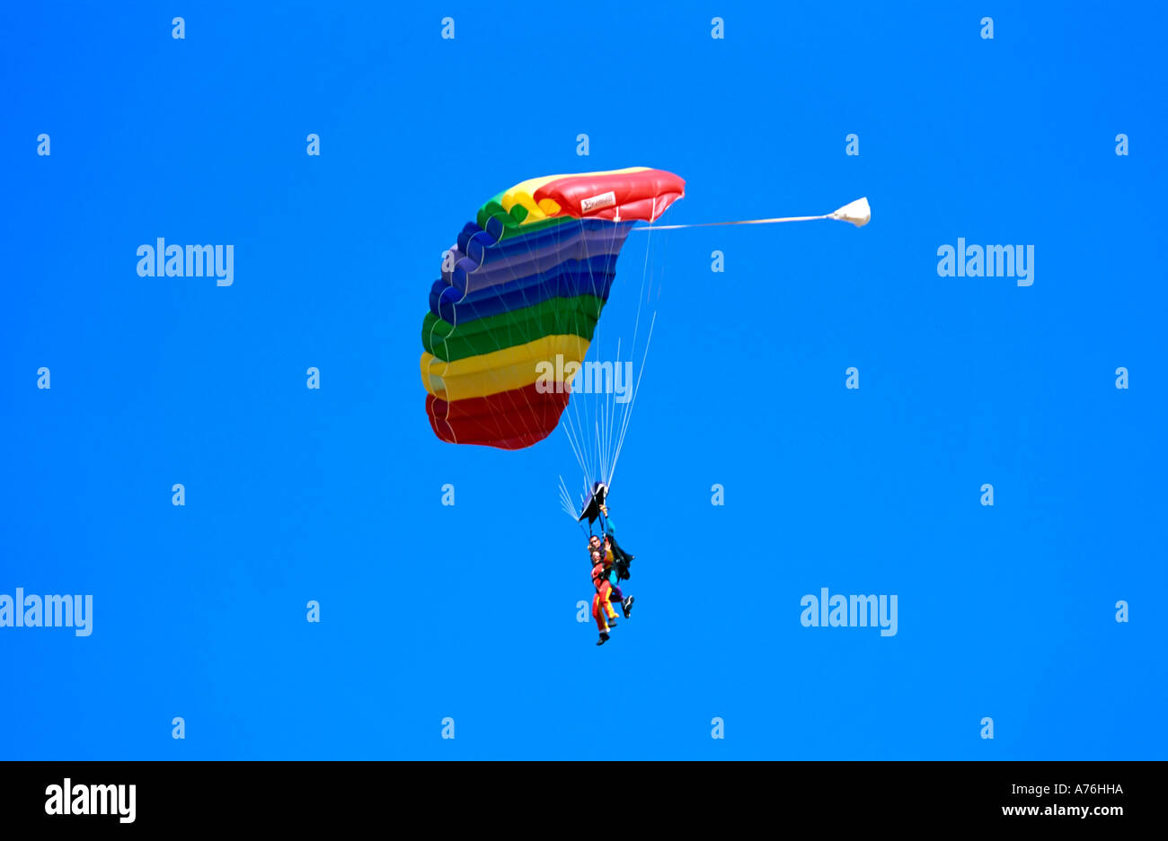 Buddy parachutists floating down in the sky with a rainbow coloured parachute and a blue sky background. Stock Photo