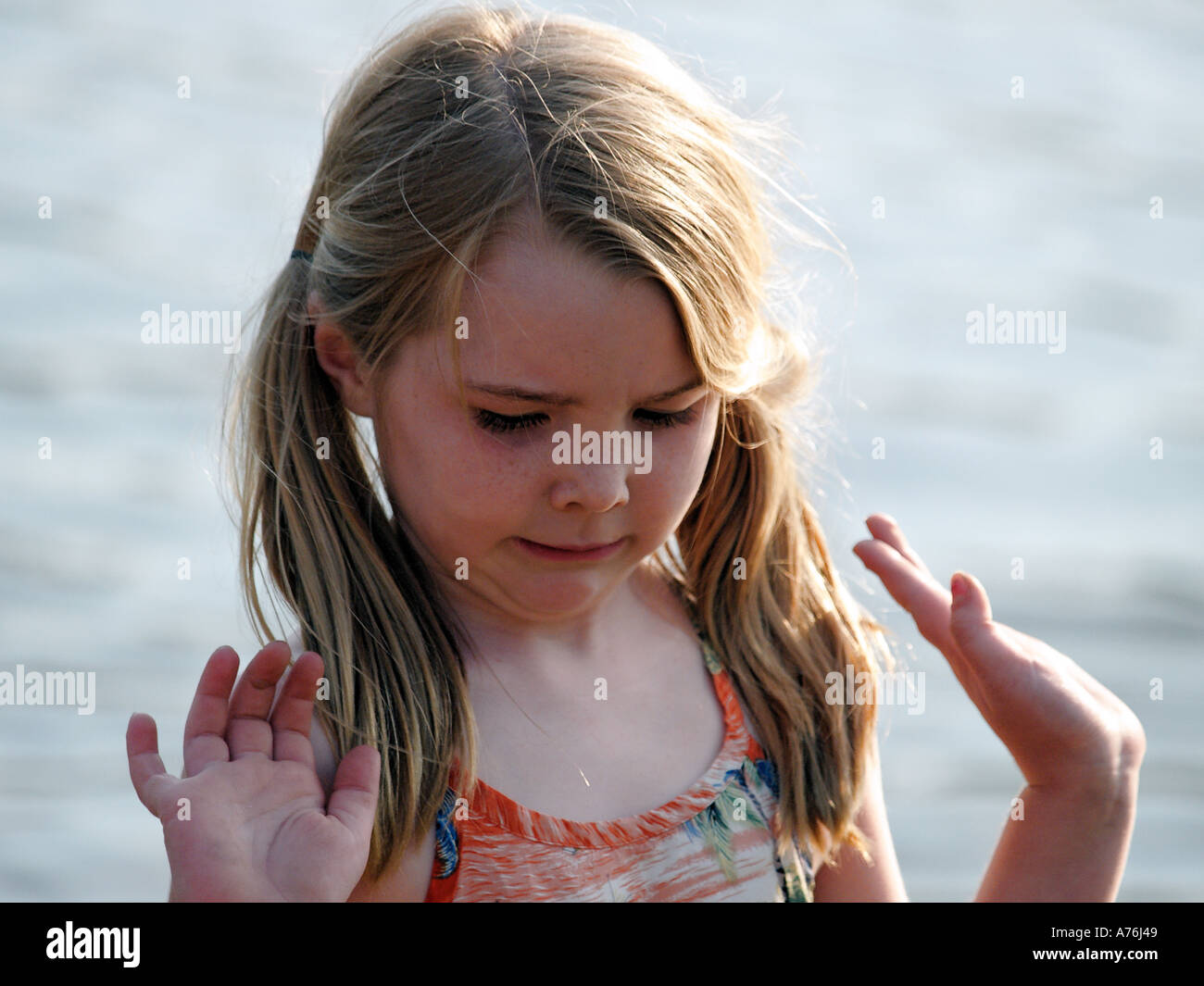 A young girl with long blonde hair plays in the sand and muck along the
