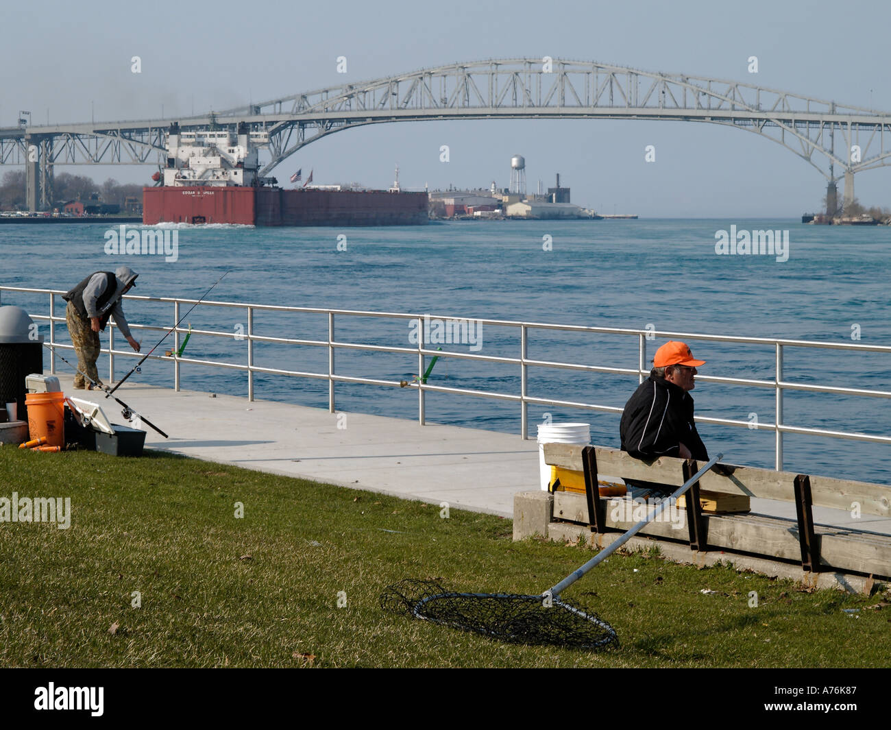 Men fishing along the St Clair River off the Port Huron MI shore Freighter Edgar B Speer steers under the Blue Water Bridge Stock Photo