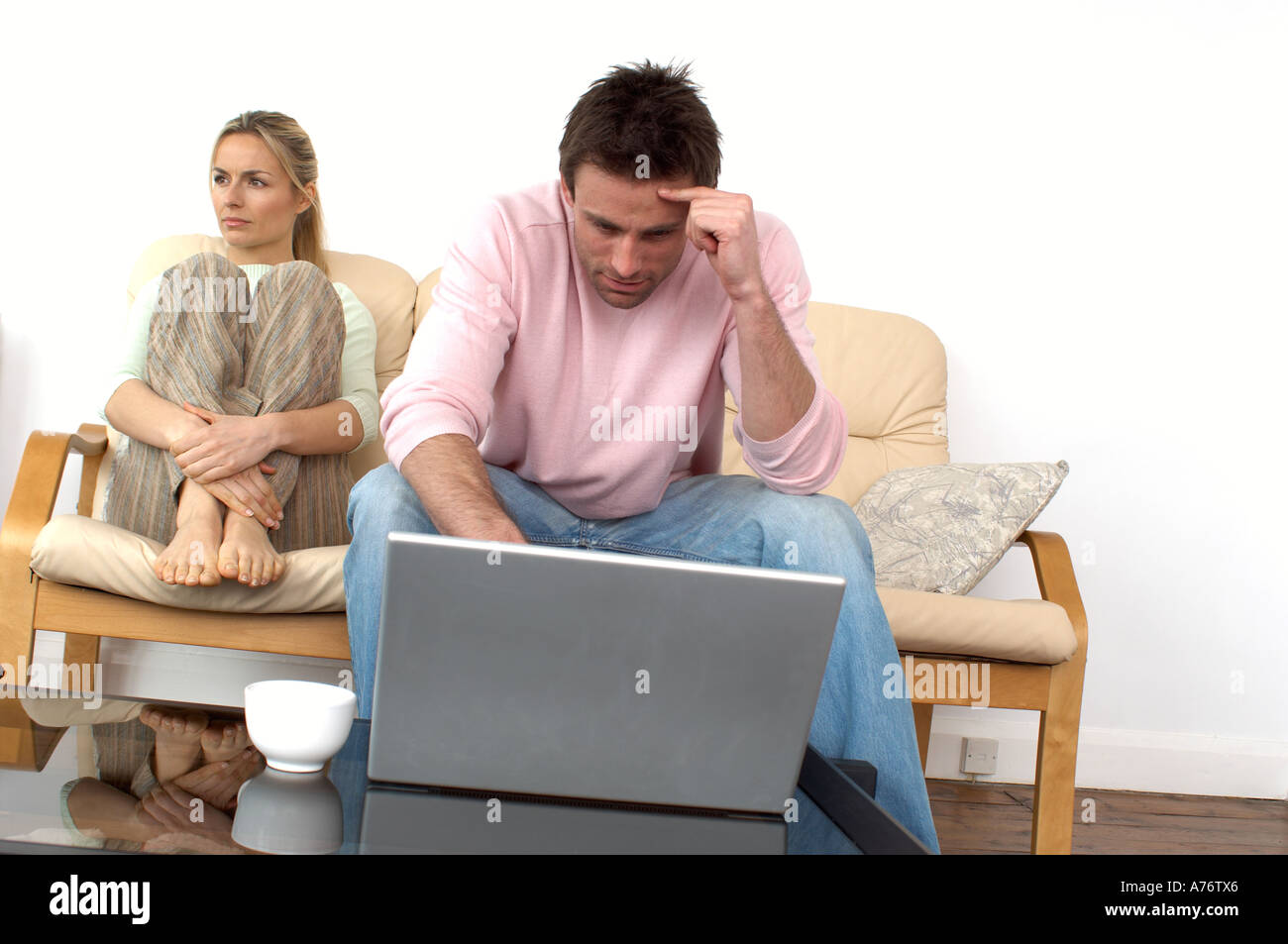 couple sitting on a sofa man looking at a laptop computer with woman looking bored Stock Photo