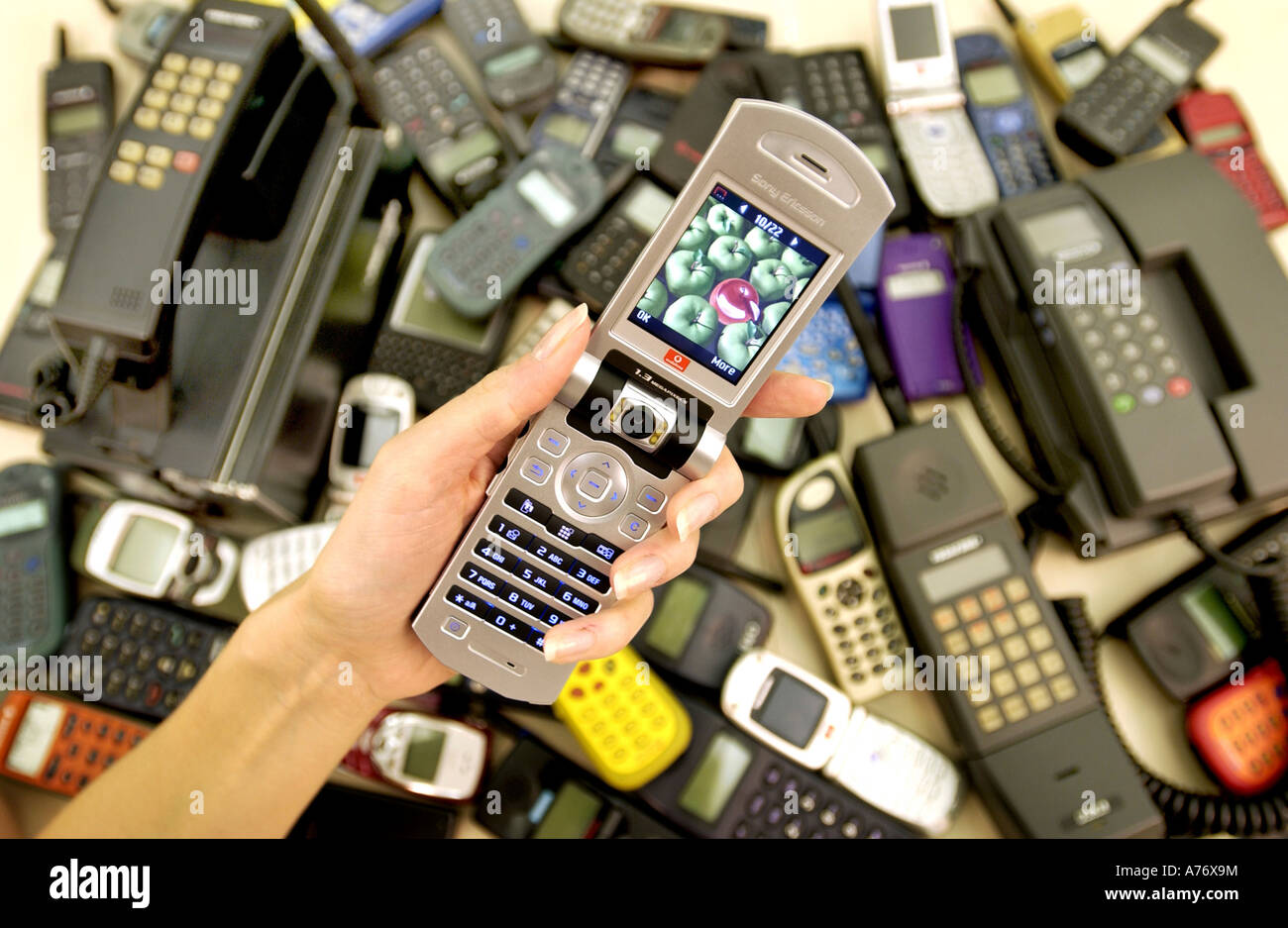 The history of mobile phones displayed with models from the 1980s to 3G videophones. A woman's hand holds a clamshell model open Stock Photo