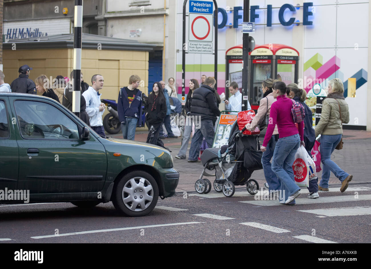 shoppers and families cross pedestrian crossing in front of stopped car whilst out christmas shopping in Belfast Christmas Eve Stock Photo