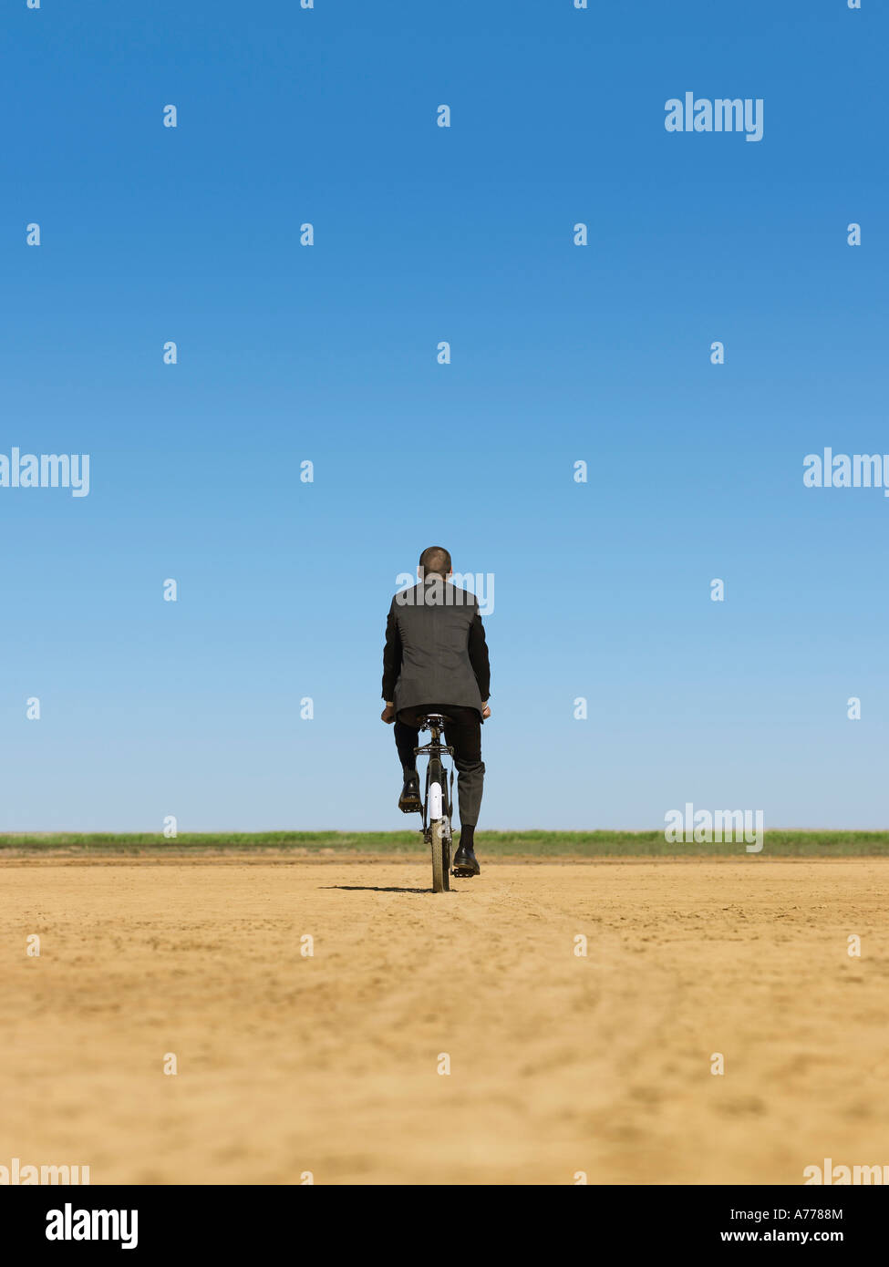 Businessman riding bicycle in desert, back view Stock Photo - Alamy