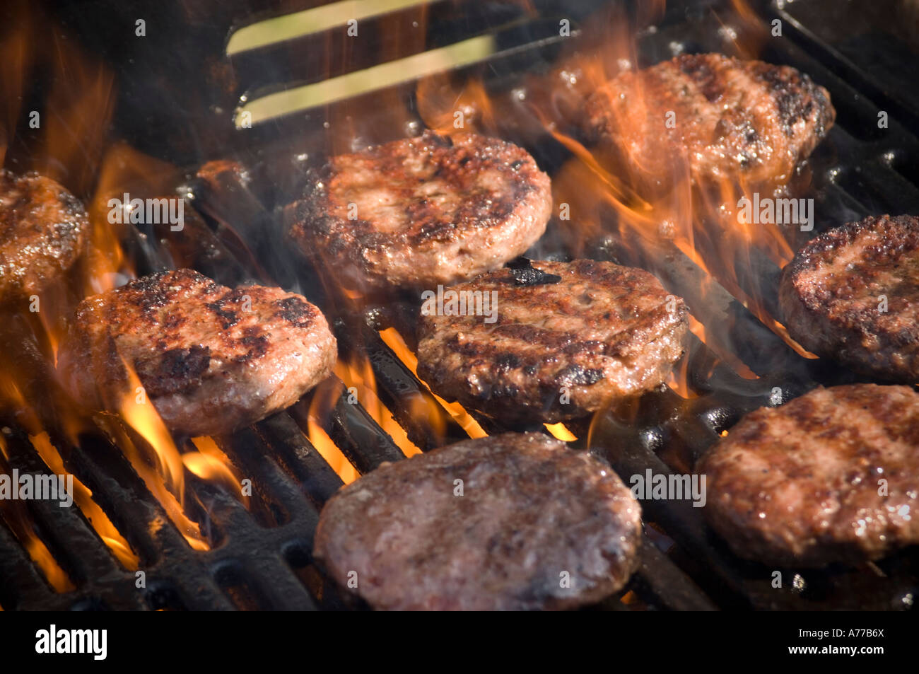Beef burgers cooking on barbecue bar-b-q summer afternoon flame grilled, UK Stock Photo