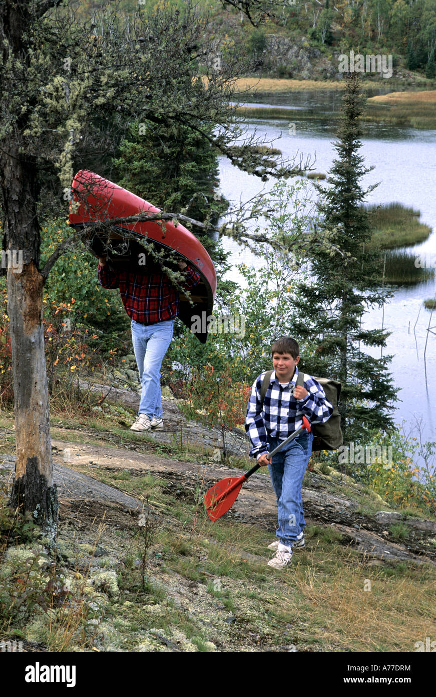 DAD AND SON PORTAGE CANOE NEAR WOOD LAKE IN THE BOUNDARY WATERS CANOE AREA WILDERNESS, NORTHERN MINNESOTA. LATE SUMMER. Stock Photo