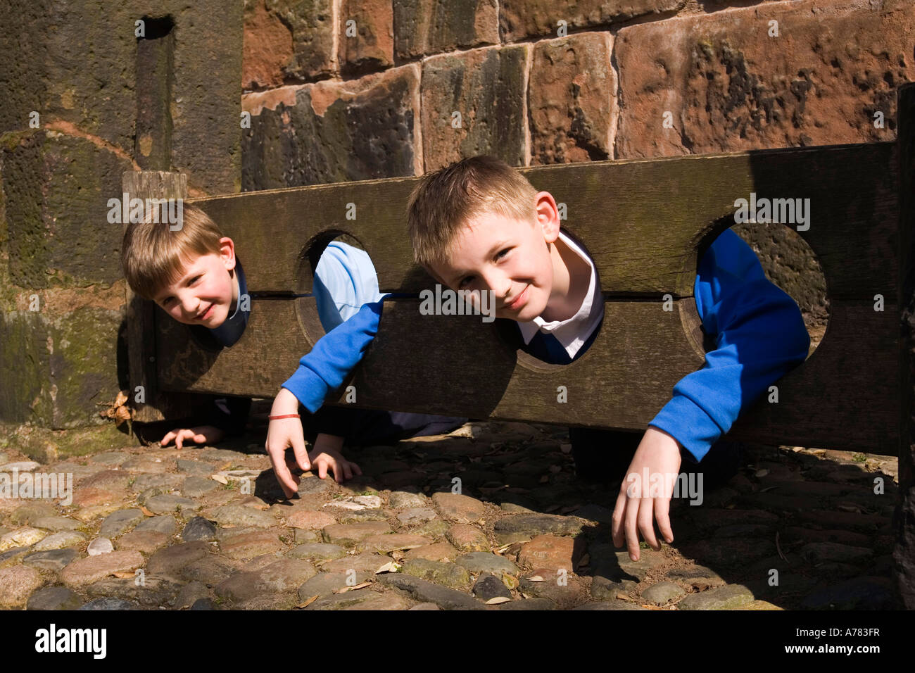 UK Cheshire Vale Royal Great Budworth two boys in village stocks at St Marys Parish church lych gate Stock Photo