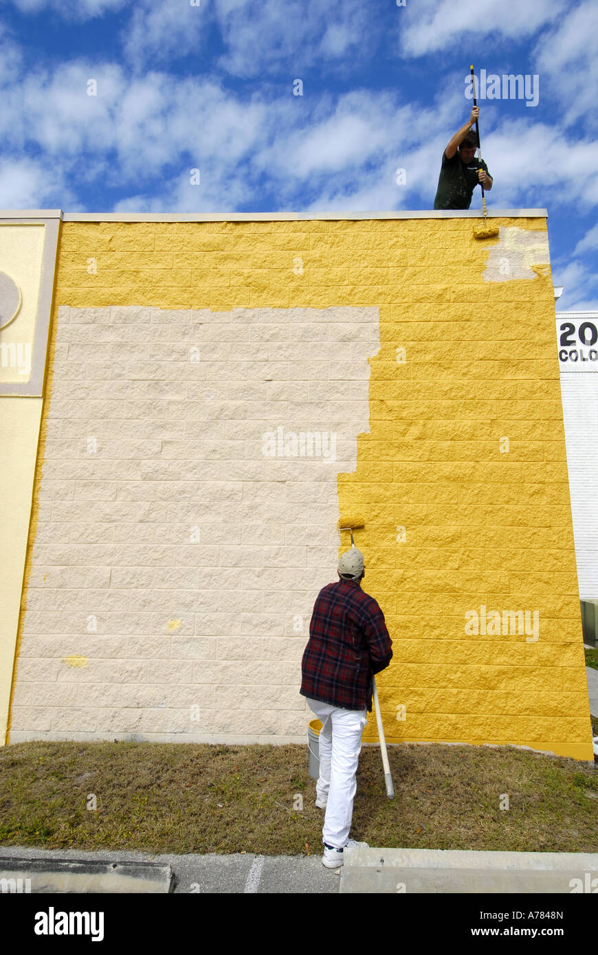 Professional painters painting a brick wall with yellow paint Stock