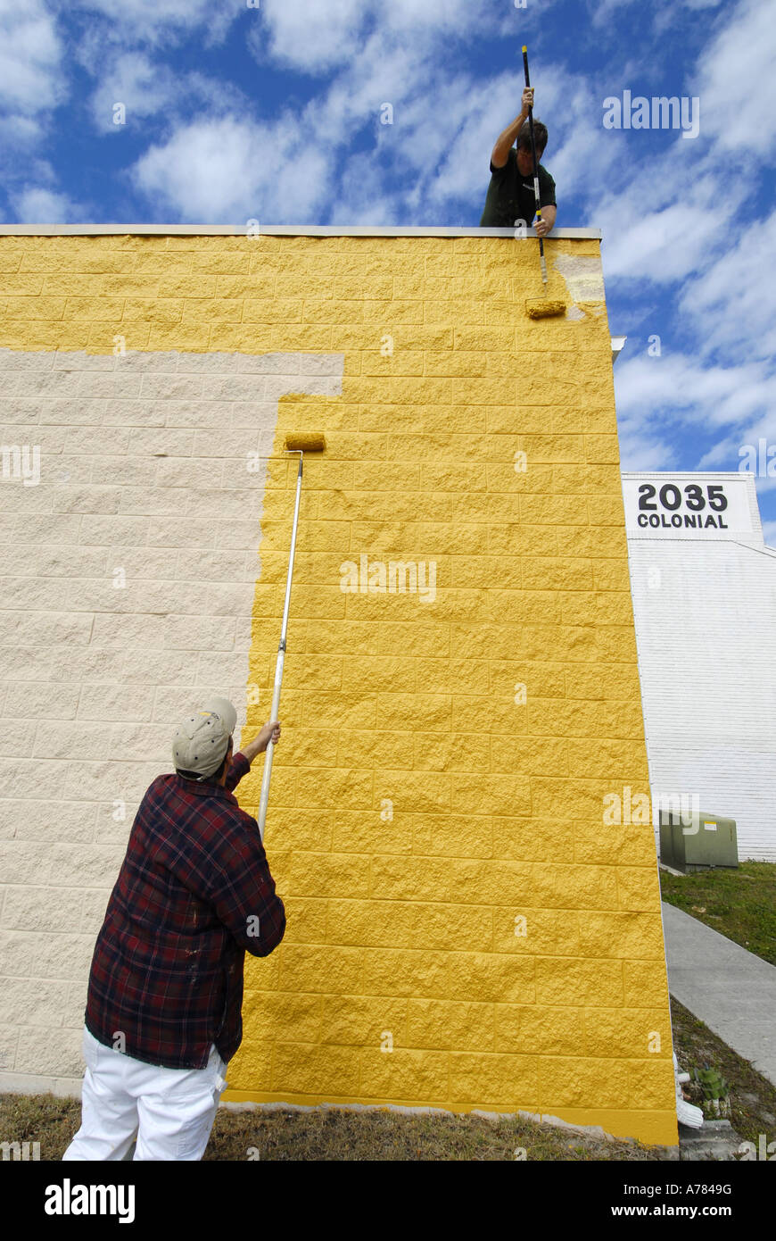 Professional painters painting a brick wall with yellow paint Stock