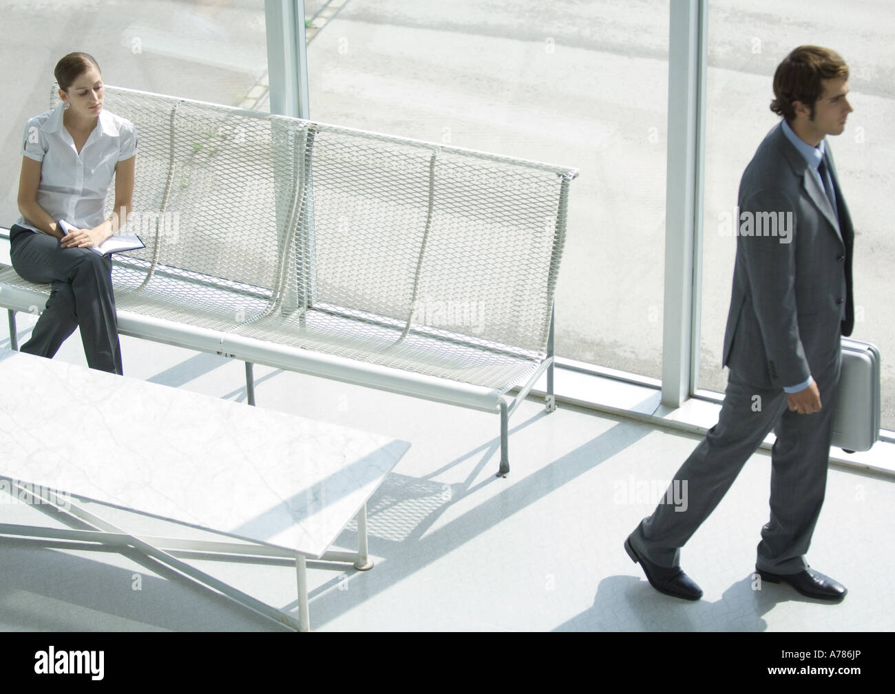 Lobby, woman sitting while businessman passes with briefcase, full length, high angle view Stock Photo