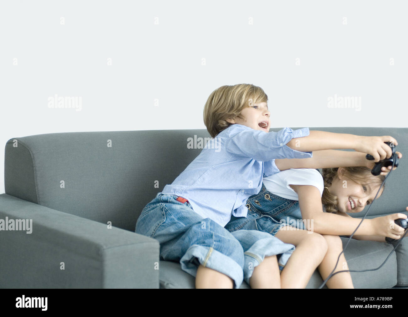 Boy and girl playing video game, holding out joysticks on sofa Stock Photo