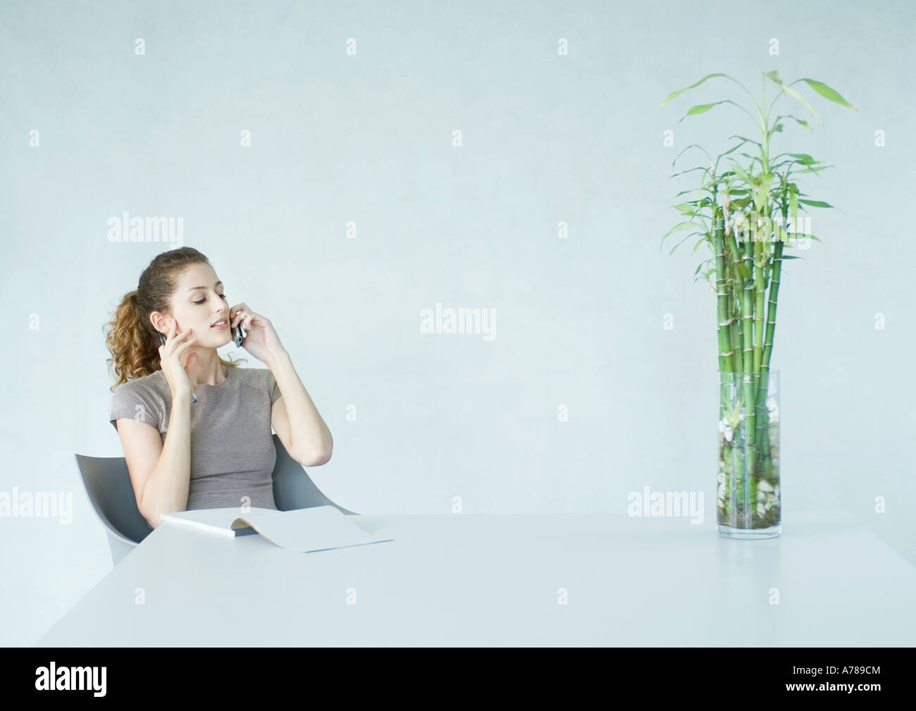 Woman using cell phone, pad of paper on table in front of her Stock Photo