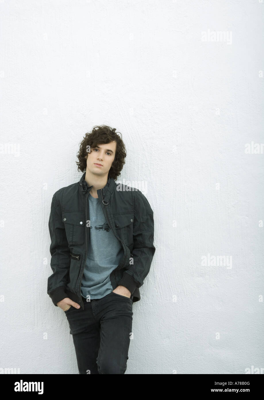 Young man leaning against wall with hands in pockets, portrait, white background Stock Photo